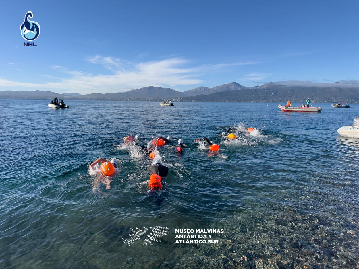 Grupo de nadadores acompañados por lanchas de seguridad, con las montañas de Bariloche de fondo