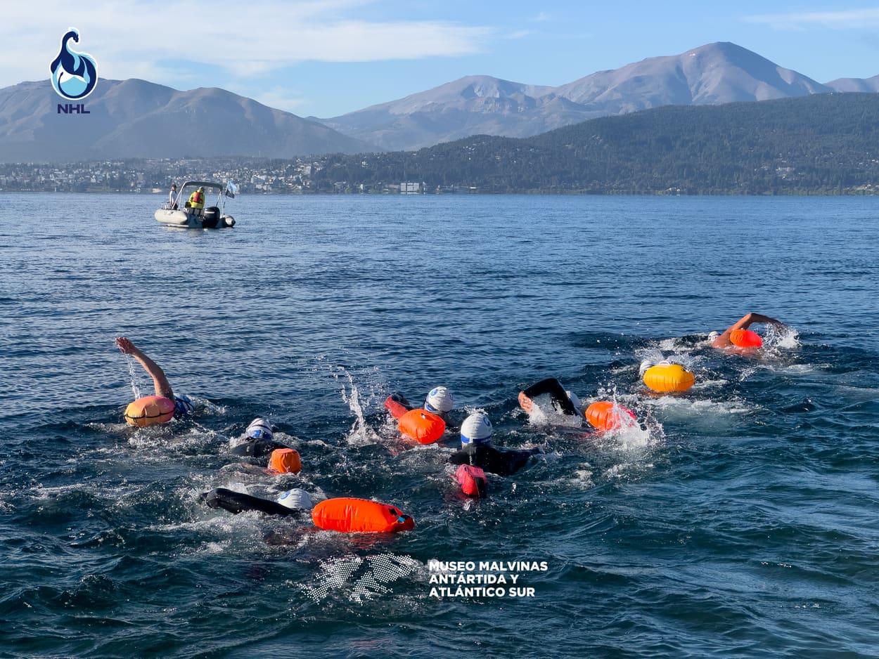 Nadadores en el cruce, con la cadena montañosa y el lago detrás