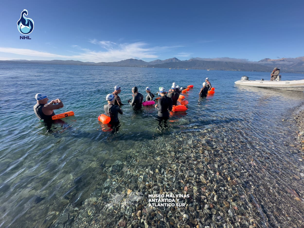 Nadadores ingresando al agua antes de la largada, con una lancha de apoyo cerca de la costa