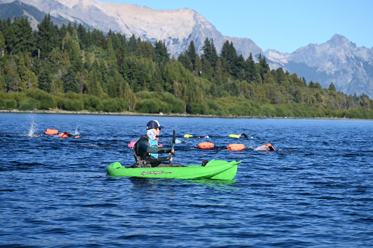 Nadadores acompañados por un kayak de seguridad, con las montañas de fondo